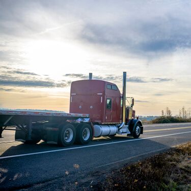 red semi-truck flatbed on two lane highway