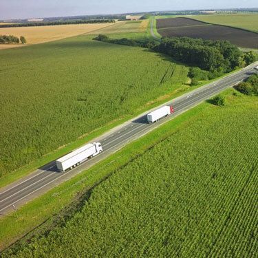 two semi-trucks driving highway with fields on both sides