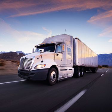 white semi-truck driving rural highway at dawn