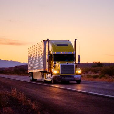 Shipping Freight from Maine to Texas - Yellow semi truckload on highway with headlights on