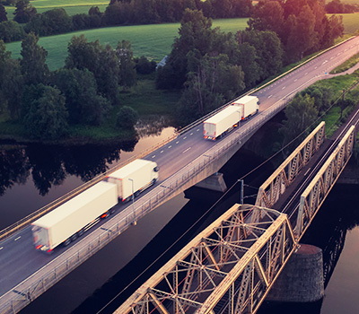 two tandem tractor trailer trucks crossing bridge over water