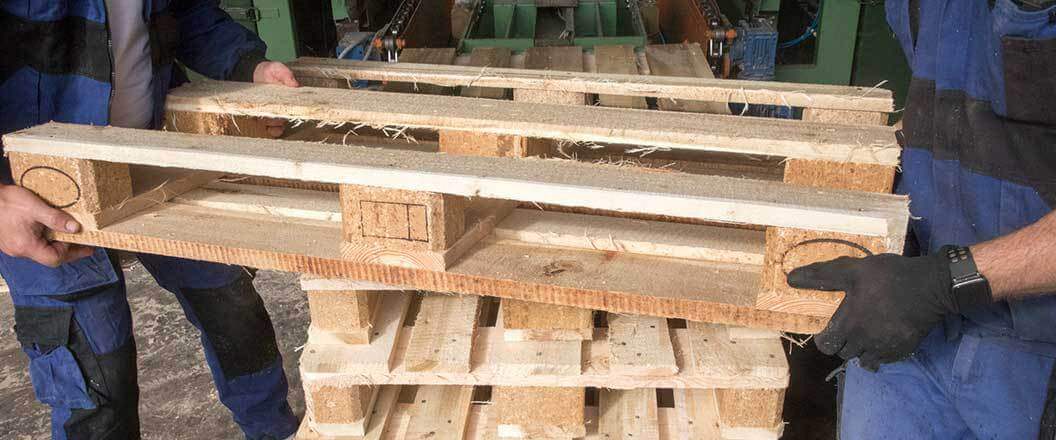 Two warehouse workers stacking pallets on top of each other 