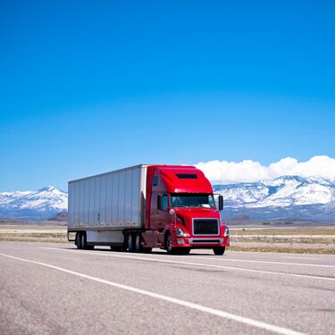 Shipping Freight from Maine to California - Red Semi truck on highway with mountains in the distance